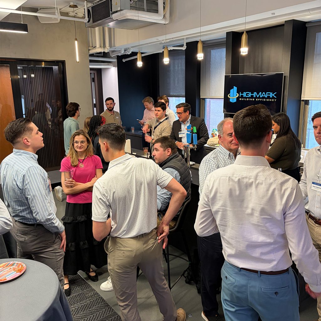 Group of professionals mingling at a corporate networking event in a modern office, with a Highmark Building Efficiency banner in the background